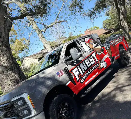 A truck with “Finest Rooter & Plumbing” branding is parked on a residential street under trees.