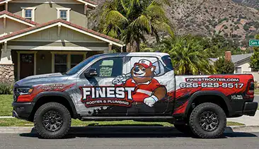 A pickup truck with a bear mascot and “Finest Rooter & Plumbing” branding, parked in front of a house. The truck displays a phone number and website.
