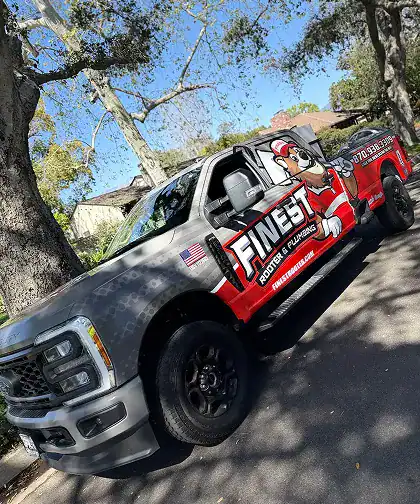 A pickup truck features “Finest Roofing & Flawless” branding on the side, with trees and houses visible in the background on a sunny day.